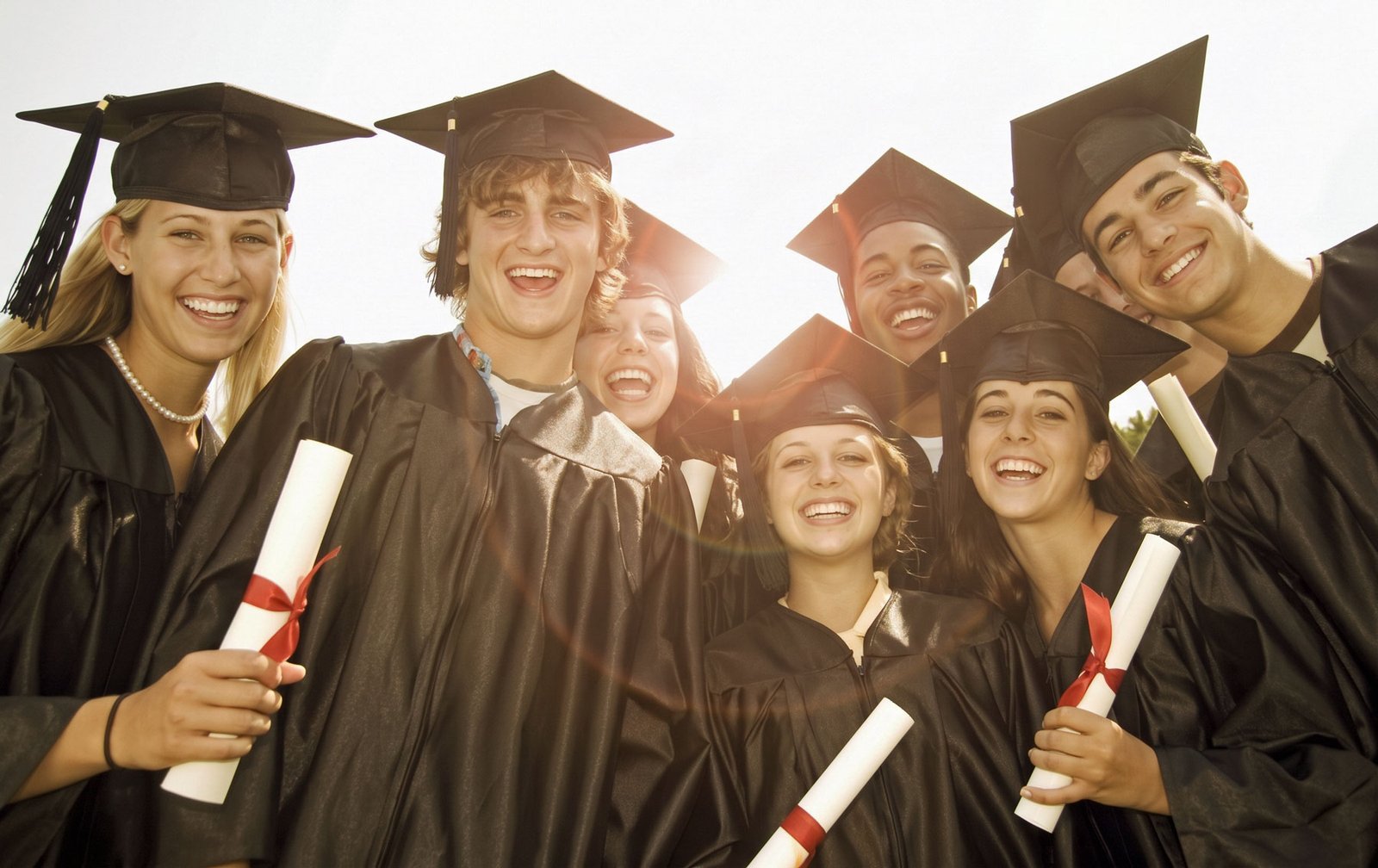 Smiling graduates in caps and gowns holding diplomas